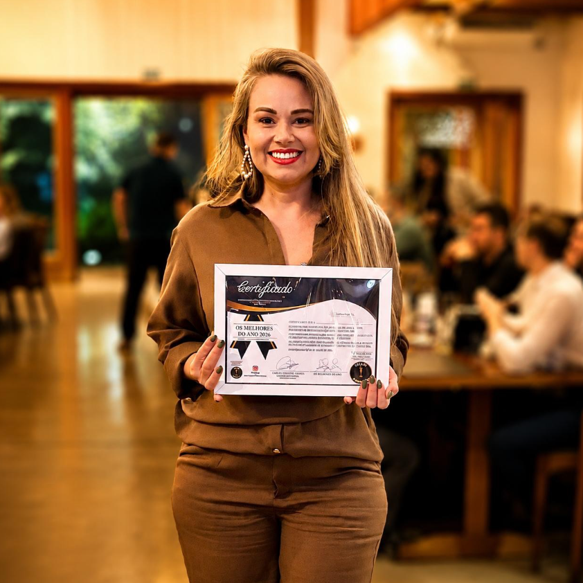 Tatiane Santos sorrindo, de blusa marrom, segurando um certificado emoldurado